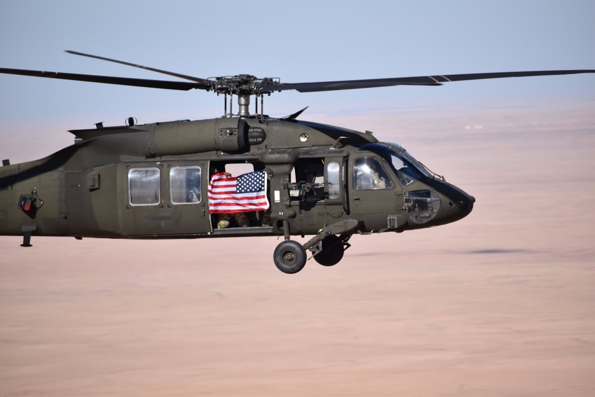 Soldiers holding the American flag in the open door of a UH-60 Black Hawk in flight